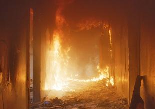 combustible materials in a tight, low-oxygen cavity are sustaining a persistent fire that behaves differently from typical interior incidents and is difficult for crews to reach. 