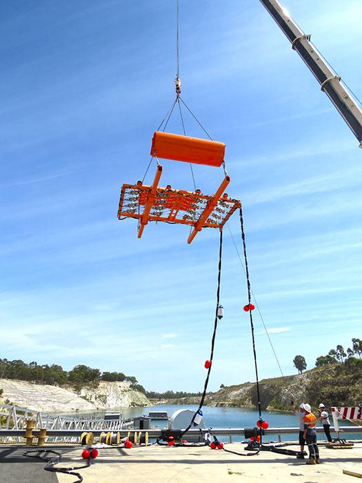 Airgun array is moved into position: Once assembled a crane lifts the array into the water before it is positioned under the shock barge which can be seen in the background.